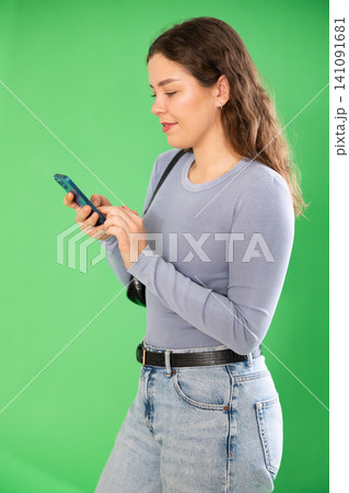 Young woman scrolling smartphone screen in front of green screen 141091681