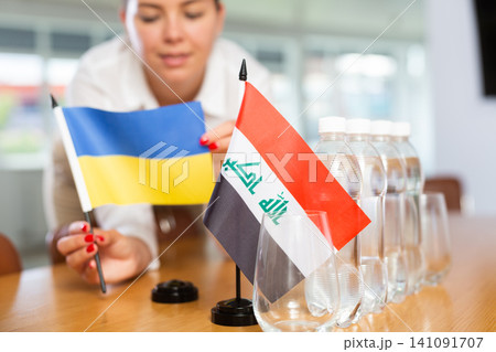Female secretary places flags of the Iraq and Ukrain flag on the table before negotiations of top political figures Female secretary places flags of the Iraq and Ukrain flag on the table before negotiations of top political figures 141091707
