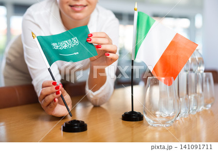 Young woman putting Saudi Arabia and Italy flags on table in office Young woman putting Saudi Arabia and Italy flags on table in office 141091711