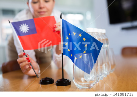 Woman secretary prepares an office for negotiations - she places flags of European Union and Taiwan table 141091715