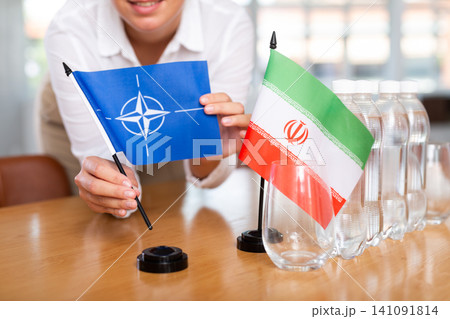 Little flag of Iran on table and flag of NATO put next to it by young woman Little flag of Iran on table and flag of NATO put next to it by young woman 141091814