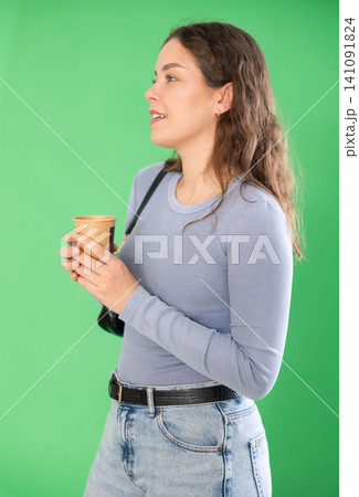 Young woman drinking coffee in front of green screen 141091824