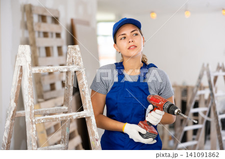 Portrait of young woman builder with drill Portrait of young woman builder with drill 141091862