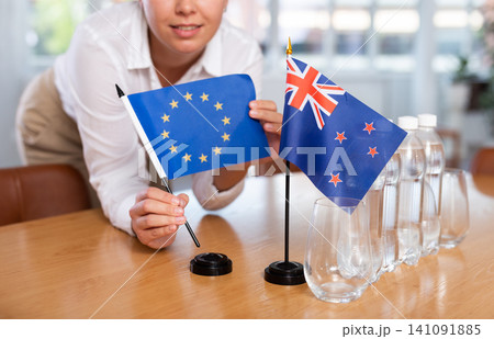 Woman secretary prepares an office for negotiations - she places flags of Australia and European Union table 141091885