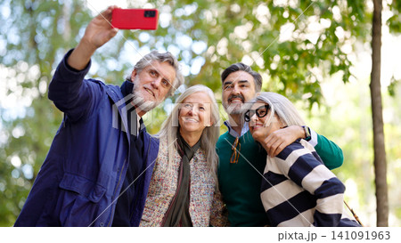 Four seniors taking group selfie with smartphone in park Four seniors taking group selfie with smartphone in park 141091963