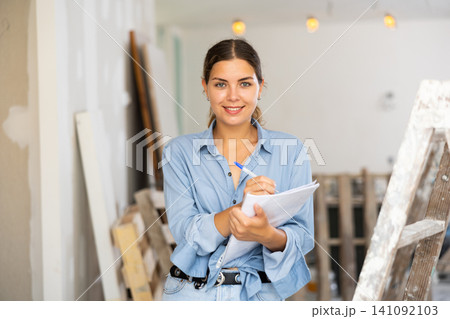 Woman with documents in her hands checks the quality of the completed repairs in cottage room Woman with documents in her hands checks the quality of the completed repairs in cottage room 141092103