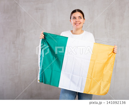 Smiling young woman holding Ireland flag Smiling young woman holding Ireland flag 141092136