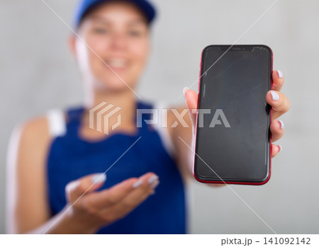 Happy female worker in work clothes showing screen of her smartphone 141092142