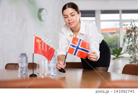 Preparing for business negotiations - woman sets small flags of countries of China and Norway on table Preparing for business negotiations - woman sets small flags of countries of China and Norway on table 141092745