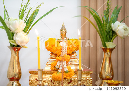 Golden Buddha statue with lotus flowers, marigold garlands, and lit candles on a peaceful Thai Buddhist 141092820