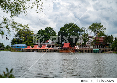Floating fish feeding rafts with traditional Thai pavilions along the riverside of Wat ThaSung, viewed from across the river with lush green trees in the background. 141092829