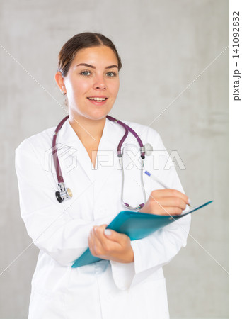 Happy female doctor standing and making notes in file 141092832