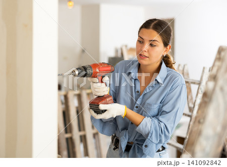 Young woman drilling a hole in the wall with screwdriver Young woman drilling a hole in the wall with screwdriver 141092842
