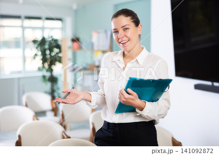 Happy european secretary woman holding folder with papers notes and inviting in auditorium Happy european secretary woman holding folder with papers notes and inviting in auditorium 141092872