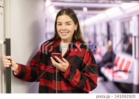 Girl is standing with phone in subway car, getting to work Girl is standing with phone in subway car, getting to work 141092920