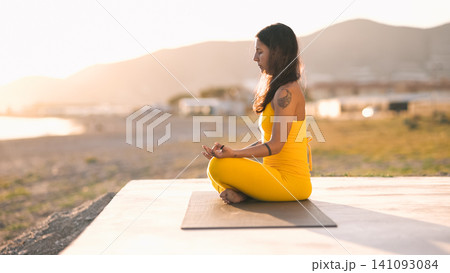 Woman meditating in lotus pose practicing yoga at sunset Woman meditating in lotus pose practicing yoga at sunset 141093084