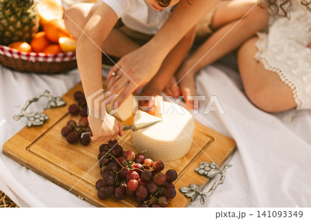 People picnic with cheese, grapes, and fruit outdoors People picnic with cheese, grapes, and fruit outdoors 141093349