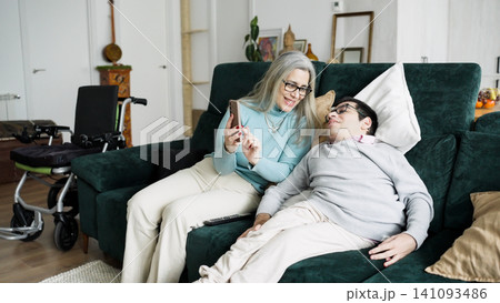 Mother and son relaxing on sofa using smartphone 141093486