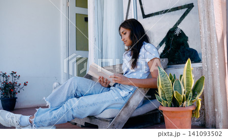 Latino woman relaxing on porch reading book Latino woman relaxing on porch reading book 141093502