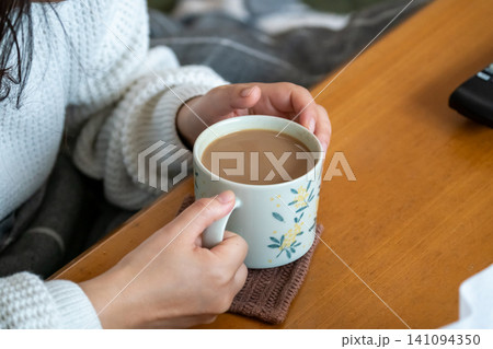花柄マグカップでカフェオレを両手で包む女性の手元 141094350
