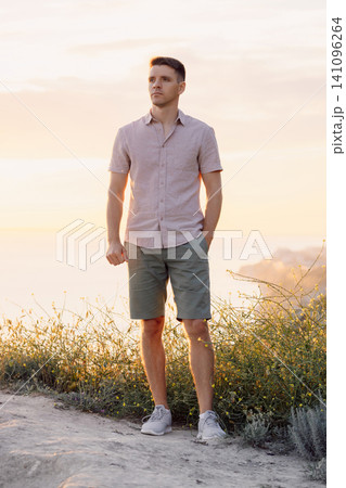 Handsome man standing in a meadow overlooking the sea during a golden hour landscape. Handsome man standing in a meadow overlooking the sea during a golden hour landscape. 141096264