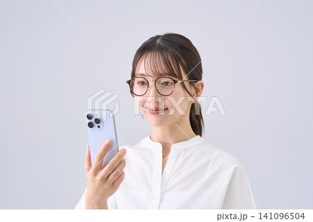 メガネをかけてスマートフォンを見る若い女性 メガネをかけてスマートフォンを見る若い女性 141096504