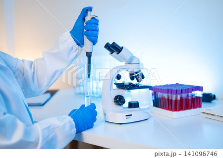 Scientist Using Pipette and Microscope in Medical Laboratory with Blood Sample Tubes Scientist Using Pipette and Microscope in Medical Laboratory with Blood Sample Tubes 141096746