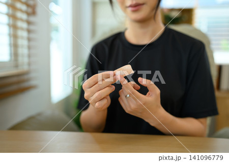 Young Asian Woman Peeling Adhesive Bandage Strip at Home, First Aid Self-Care Concept Young Asian Woman Peeling Adhesive Bandage Strip at Home, First Aid Self-Care Concept 141096779
