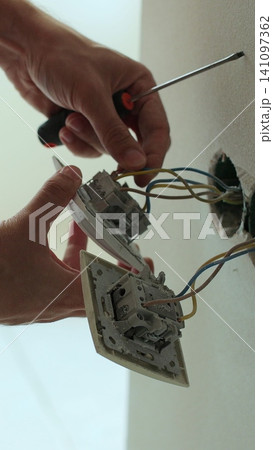 Vertical video Professional electrician working on a home electrical system. Close up man installing a wall socket at new apartment or house. 141097362