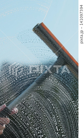 Vertical video Woman hands wipes with a scraper dirty window close up. Washes a window, glass with a brush. Concentration of cleanliness, cleaning companies. Vertical video Woman hands wipes with a scraper dirty window close up. Washes a window, glass with a brush. Concentration of cleanliness, cleaning companies. 141097394