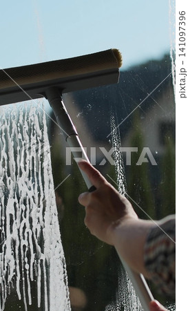 Vertical video Woman wipes with a scraper dirty window close up. Washes a window, glass with a brush. Concentration of cleanliness, cleaning companies. Vertical video Woman wipes with a scraper dirty window close up. Washes a window, glass with a brush. Concentration of cleanliness, cleaning companies. 141097396