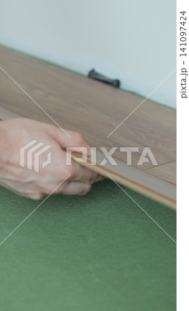 Vertical video Man lays laminate flooring on the floor in a room. Repair of the floor of the house. Vertical video Man lays laminate flooring on the floor in a room. Repair of the floor of the house. 141097424
