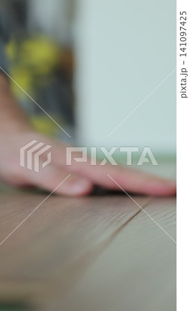 Vertical video Man kneeling and installing wood laminate floor in a home. Closeup on male hands. Vertical video Man kneeling and installing wood laminate floor in a home. Closeup on male hands. 141097425