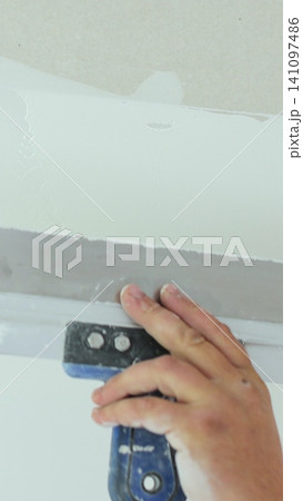 Vertical video Plastering a concrete wall with putty using a large spatula. The master of apartment renovation levels the walls with starting plaster. The internal construction and finishing work. Vertical video Plastering a concrete wall with putty using a large spatula. The master of apartment renovation levels the walls with starting plaster. The internal construction and finishing work. 141097486