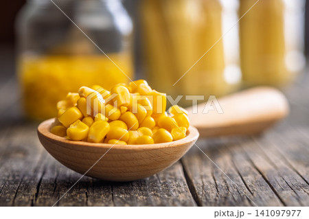 Canned Sweet Corn Kernels in a Wooden Spoon on Rustic Table With Blurred Jars Background 141097977