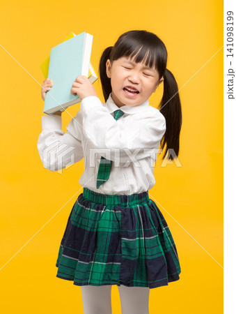 a frustrated young student in uniform holding books against a bright yellow background. 141098199