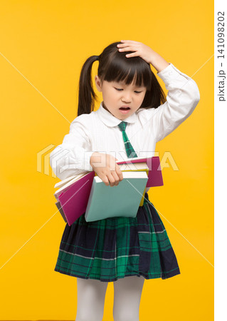 a confused schoolgirl scratching her head while holding textbooks against a yellow background. 141098202