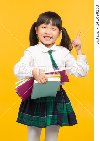 happy Asian school girl holding book on yellow background, smiling child in school uniform, education concept 141098203