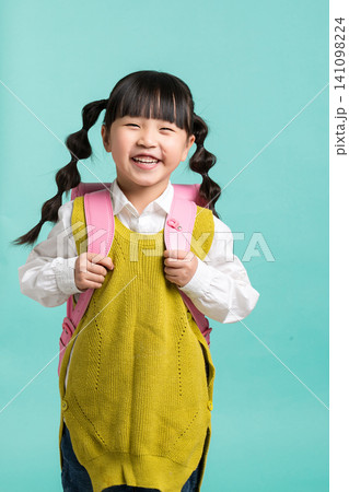 a cheerful Asian female student, with her hair in gourd braids and carrying a pink backpack, stands against a blue-green background with a back-to-school theme. a cheerful Asian female student, with her hair in gourd braids and carrying a pink backpack, stands against a blue-green background with a back-to-school theme. 141098224