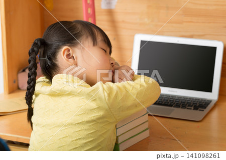 a tired little girl sleeping peacefully on a stack of books next to a laptop. a tired little girl sleeping peacefully on a stack of books next to a laptop. 141098261