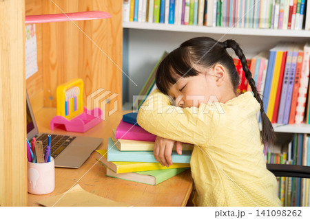 a tired little girl sleeping peacefully on a stack of books next to a laptop. a tired little girl sleeping peacefully on a stack of books next to a laptop. 141098262