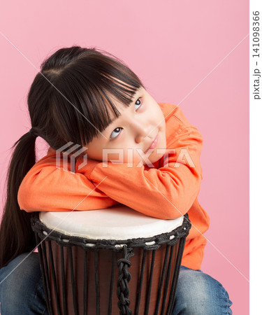 Cute Asian little girl playing drum, smiling child with percussion instrument on pink background, music education concept Cute Asian little girl playing drum, smiling child with percussion instrument on pink background, music education concept 141098366