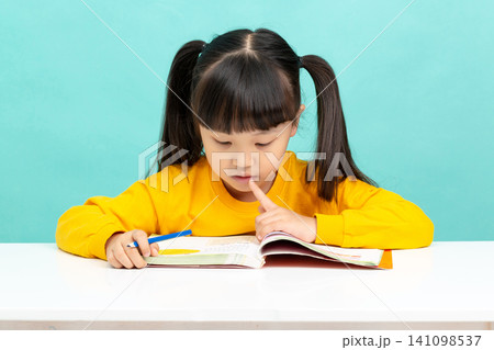 An Asian female student is reading in a blue background. Her expression is serious and focused, suggesting she may have learning difficulties. An Asian female student is reading in a blue background. Her expression is serious and focused, suggesting she may have learning difficulties. 141098537