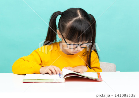 An Asian female student is reading in a blue background. Her expression is serious and focused, suggesting she may have learning difficulties. An Asian female student is reading in a blue background. Her expression is serious and focused, suggesting she may have learning difficulties. 141098538