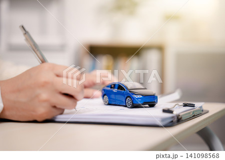 Person signing vehicle purchase contract with toy car on document, finalizing auto loan lease and insurance agreement at dealership for ownership in automotive finance office Person signing vehicle purchase contract with toy car on document, finalizing auto loan lease and insurance agreement at dealership for ownership in automotive finance office 141098568