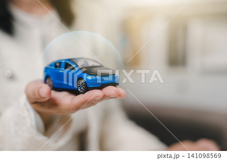 Woman hand holding blue toy car under protective shield for auto insurance service, protecting vehicle from accident or damage with secure commercial transport contract Woman hand holding blue toy car under protective shield for auto insurance service, protecting vehicle from accident or damage with secure commercial transport contract 141098569
