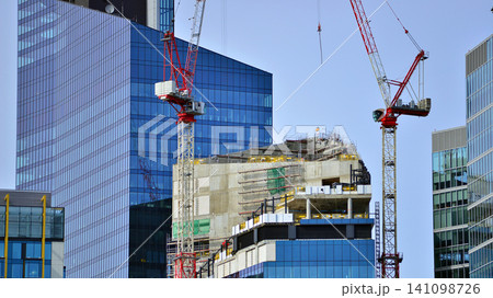 Crane on the construction site in a site surrounded by the high buildings. Office building under construction in the vicinity of high apartment buildings and office building. Crane on the construction site in a site surrounded by the high buildings. Office building under construction in the vicinity of high apartment buildings and office building. 141098726