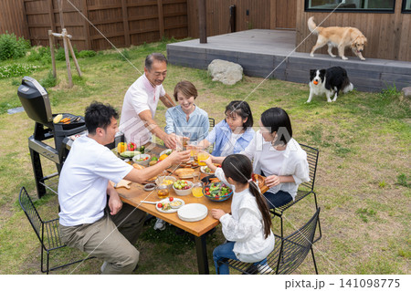 庭でバーベキューを楽しみながら乾杯する三世代の家族と愛犬 庭でバーベキューを楽しみながら乾杯する三世代の家族と愛犬 141098775