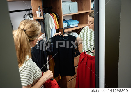 Woman choosing outfit in wardrobe mirror Woman choosing outfit in wardrobe mirror 141098800