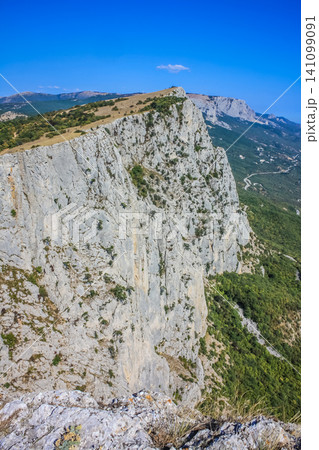 Mediterranean landscape. Forested rocks of the Black Sea coast of the southern coast of the Crimean Peninsula on a clear sunny day. View down from the rocky mountains to the sea Mediterranean landscape. Forested rocks of the Black Sea coast of the southern coast of the Crimean Peninsula on a clear sunny day. View down from the rocky mountains to the sea 141099091